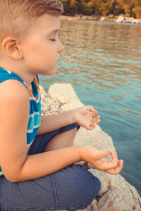 Side view of boy meditating by lake