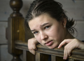 Portrait of depressed girl leaning on wooden railing at home