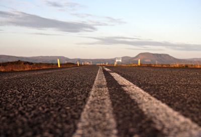 Empty road leading towards mountains against sky during sunset