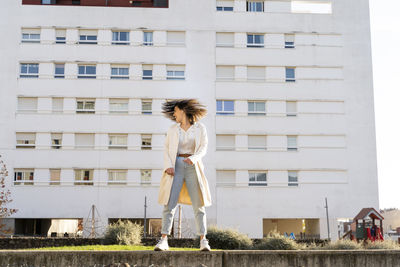 Happy businesswoman shaking head while standing against building in garden