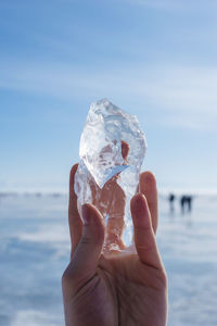 Close-up of hand holding ice over sea against sky