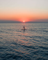 Silhouette man in sea against sky during sunset