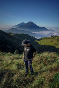 Rear view of man standing on field against mountain