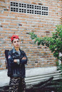 Portrait of young man with arms crossed standing against brick wall