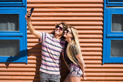 Friends taking selfie while standing against house during summer