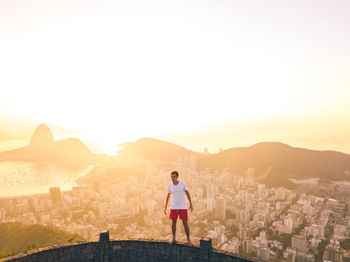 Full length of man standing in city against sky during sunset