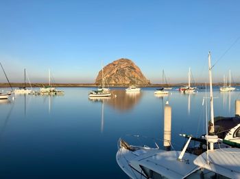 Sailboats moored in sea against clear blue sky