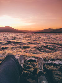 Low section of man in sea against sky during sunset