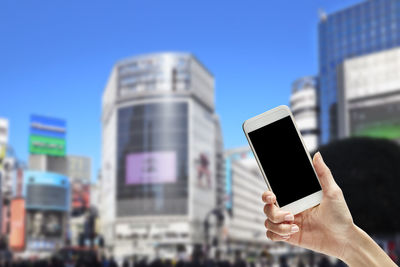 Close-up of hand holding smart phone against city buildings