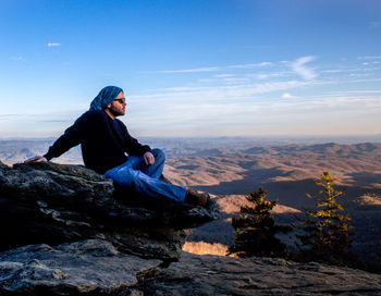 Full length of young man sitting on rock against sky