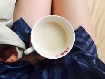 Low section of woman holding coffee cup on bed