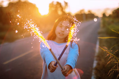 Portrait of teenage girl holding fireworks on road