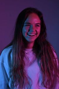 Smiling teenage girl looking away while standing over purple background