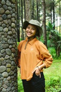 Portrait of smiling young woman standing against stone wall