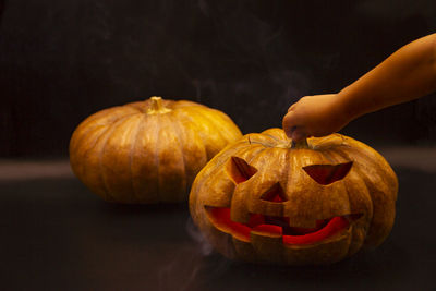 Close-up of hand holding pumpkin against black background