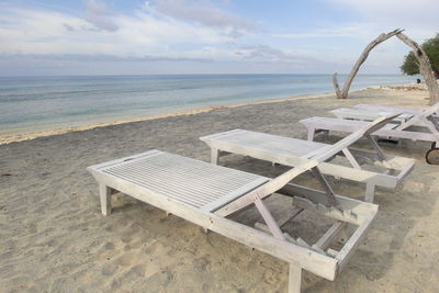 Deck chairs on beach against sky