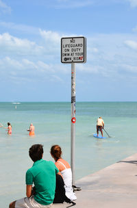 People sitting by sea against sky