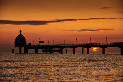Silhouette bridge over sea against sky during sunset
