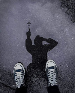 Low section of man in canvas shoes standing on wet street