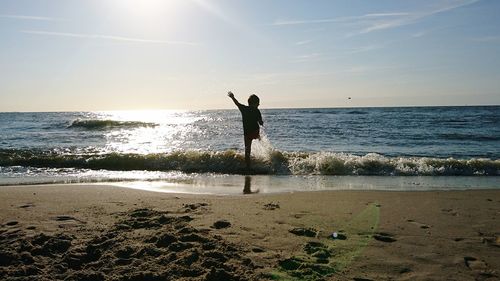 Silhouette boy playing at beach against sky during sunset