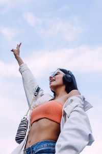 Low angle portrait of young woman against sky