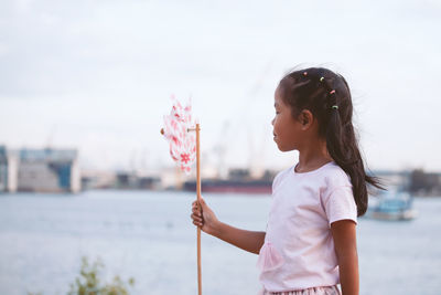 Girl holding pinwheel toy at beach against sky