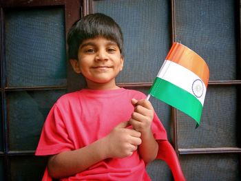 Portrait of smiling boy holding indian flag against window