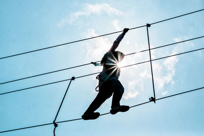 Low angle view of woman walking on tightrope against sky