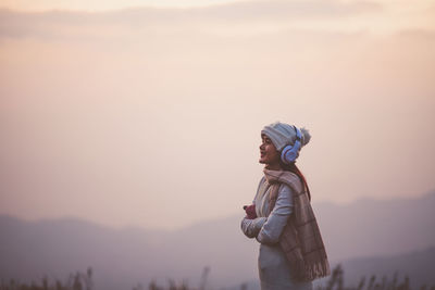 Side view of woman standing against sky during sunset