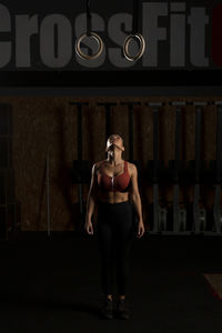 Full body of young fit lady in sportswear standing in modern gym and looking up before training on gymnastic rings