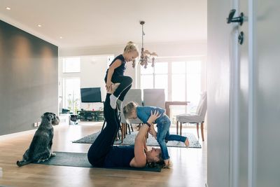 Smiling mother lifting happy daughters while lying on exercise mat at home