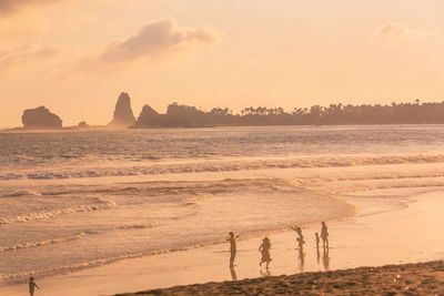 People on beach against sky during sunset