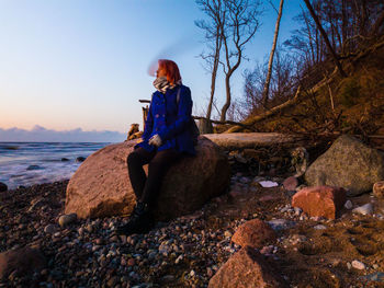 Man sitting on rock against sky