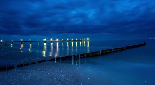Pier over sea against blue sky at night