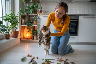 Pet owner holding idle lazy cat trying to stimulate interest, activity with natural objects on floor