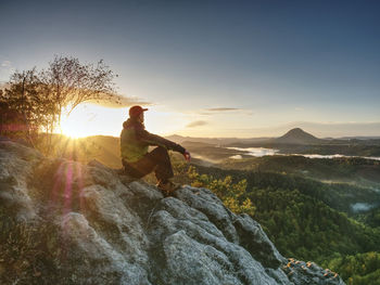 Man take rest on peak. traveler with green windproof jacket resting on ground and admires peaks