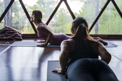 Woman doing yoga while looking at female fitness instructor in health retreat