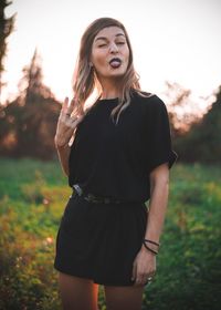 Woman gesturing peace sign while sticking out tongue on field