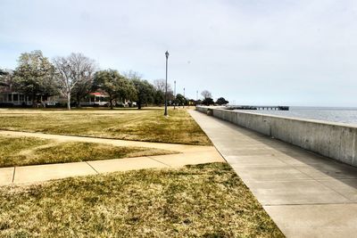 Scenic view of park next to sea against cloudy sky