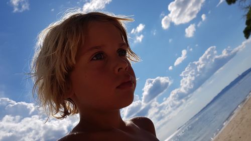 Tilt image of cute boy looking away at beach against sky during summer