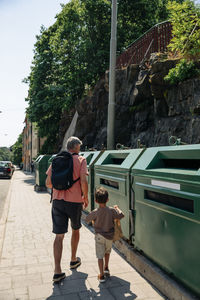 Rear view of grandfather and grandson walking towards garbage bins