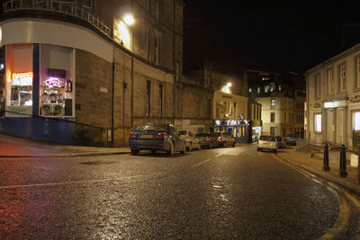 Cars on street by illuminated buildings in city at night