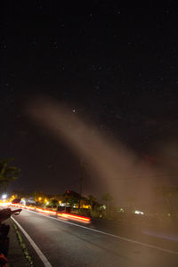 Illuminated street amidst buildings against sky at night