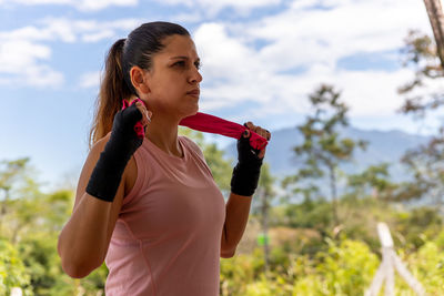 Young woman looking away while standing against sky