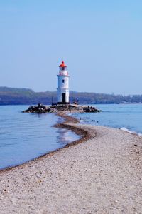 Lighthouse by sea against clear sky