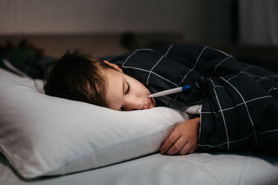 Sad child laying in bed with thermometer in his mouth. temperature measurement. sick boy on bed late