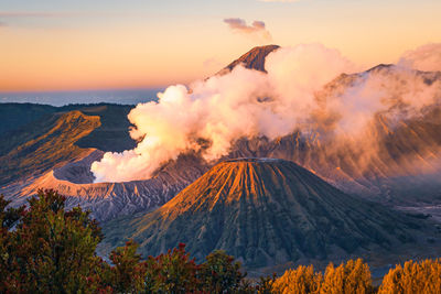 Panoramic view of smoke emitting from volcanic mountain against sky during sunset