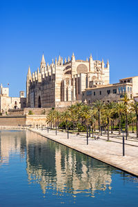 Buildings by river against clear blue sky