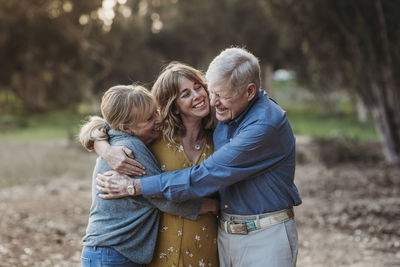 Portrait of adult woman and senior parents hugging at park