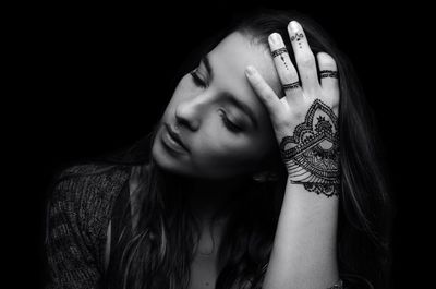 Close-up of young woman with henna tattoo against black background